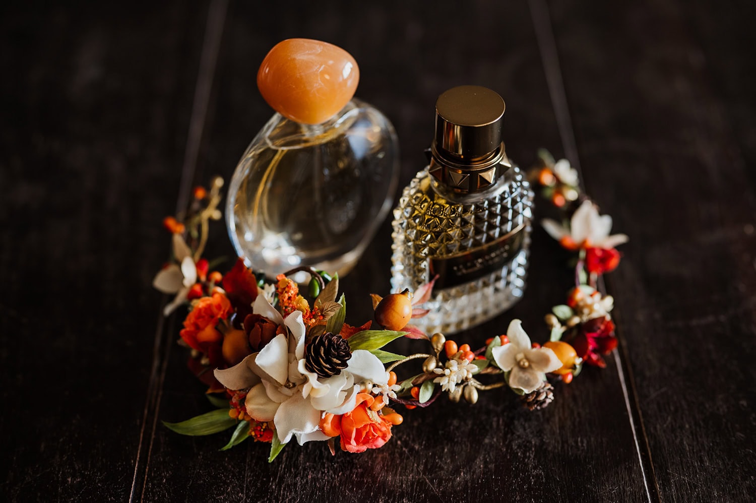 Two elegant perfume bottles are surrounded by a floral crown on a dark wooden surface.