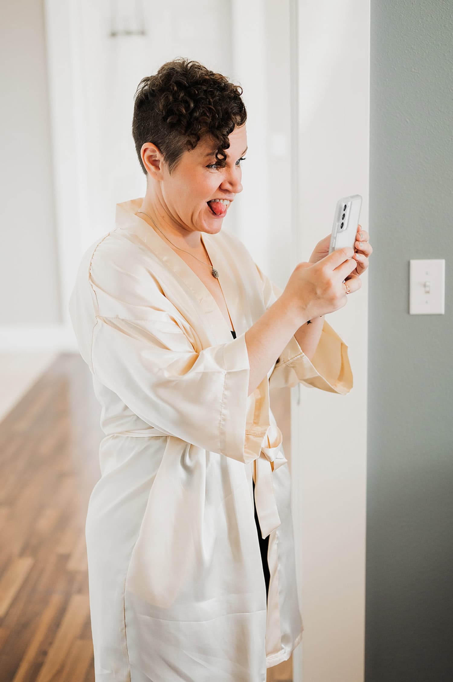A person in a robe takes an excited selfie with a smartphone in a bright room, celebrating their wedding at Gorge Crest Vineyards.