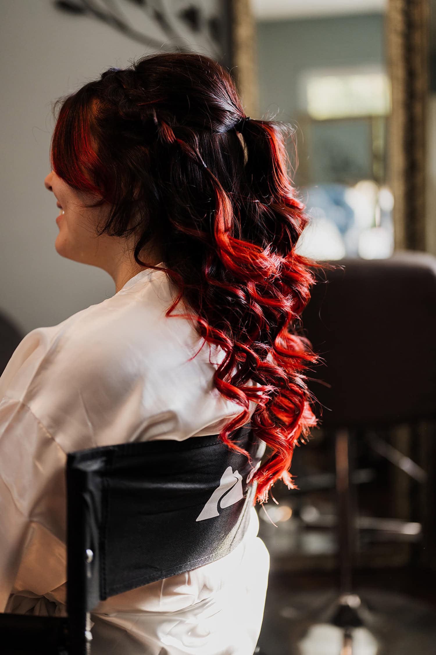 A bride with long, curly red and black hair sits in a salon chair, waiting for her transformation.