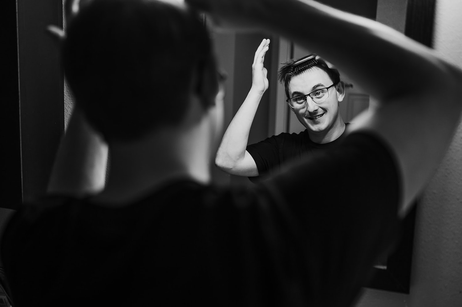 A man stands in front of a mirror at Gorge Crest Vineyards, adjusting his hair and smiling, captured in a black and white photograph.