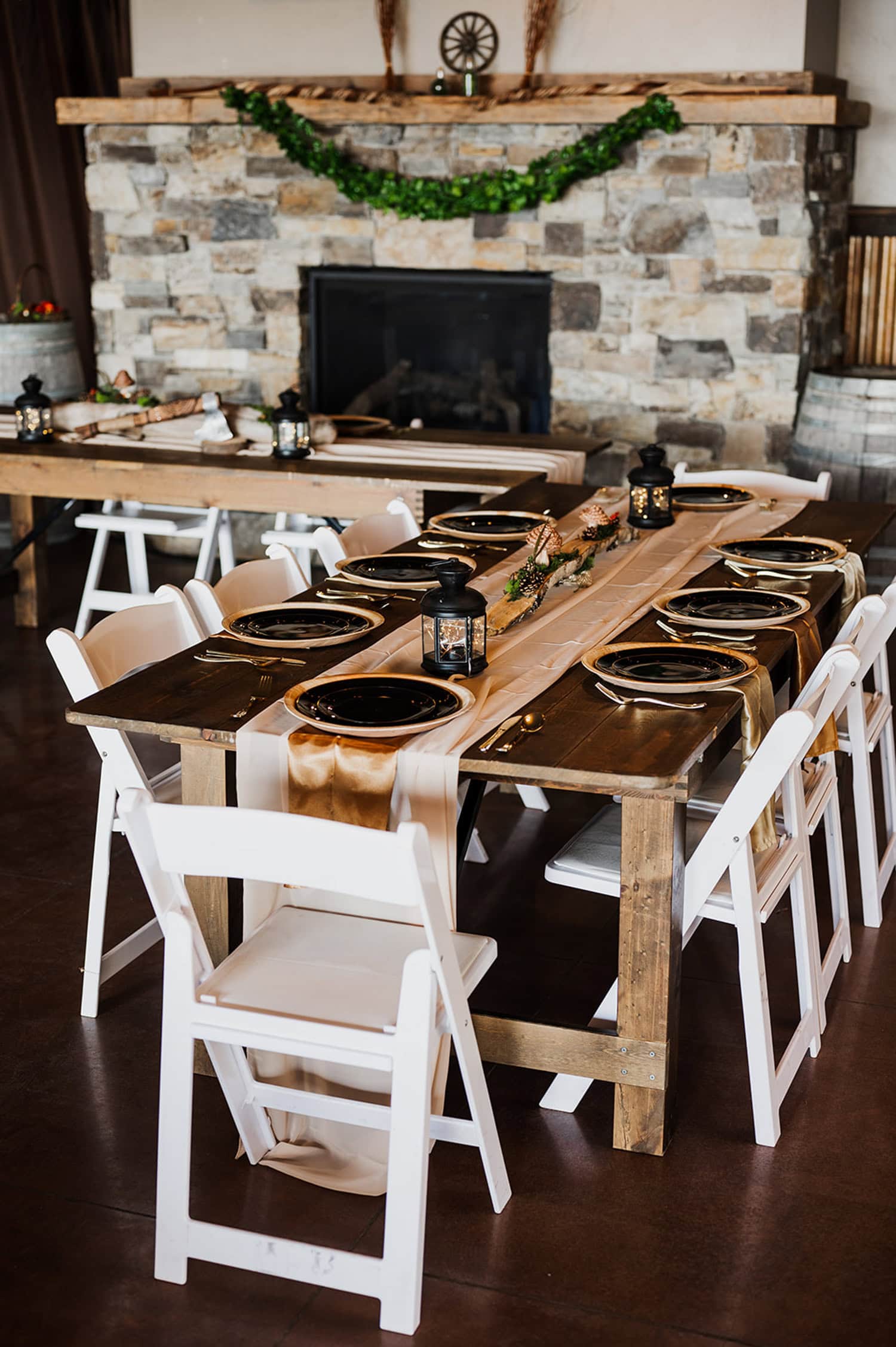 An elegant dining table with black plates and white chairs is set in front of a stone fireplace.