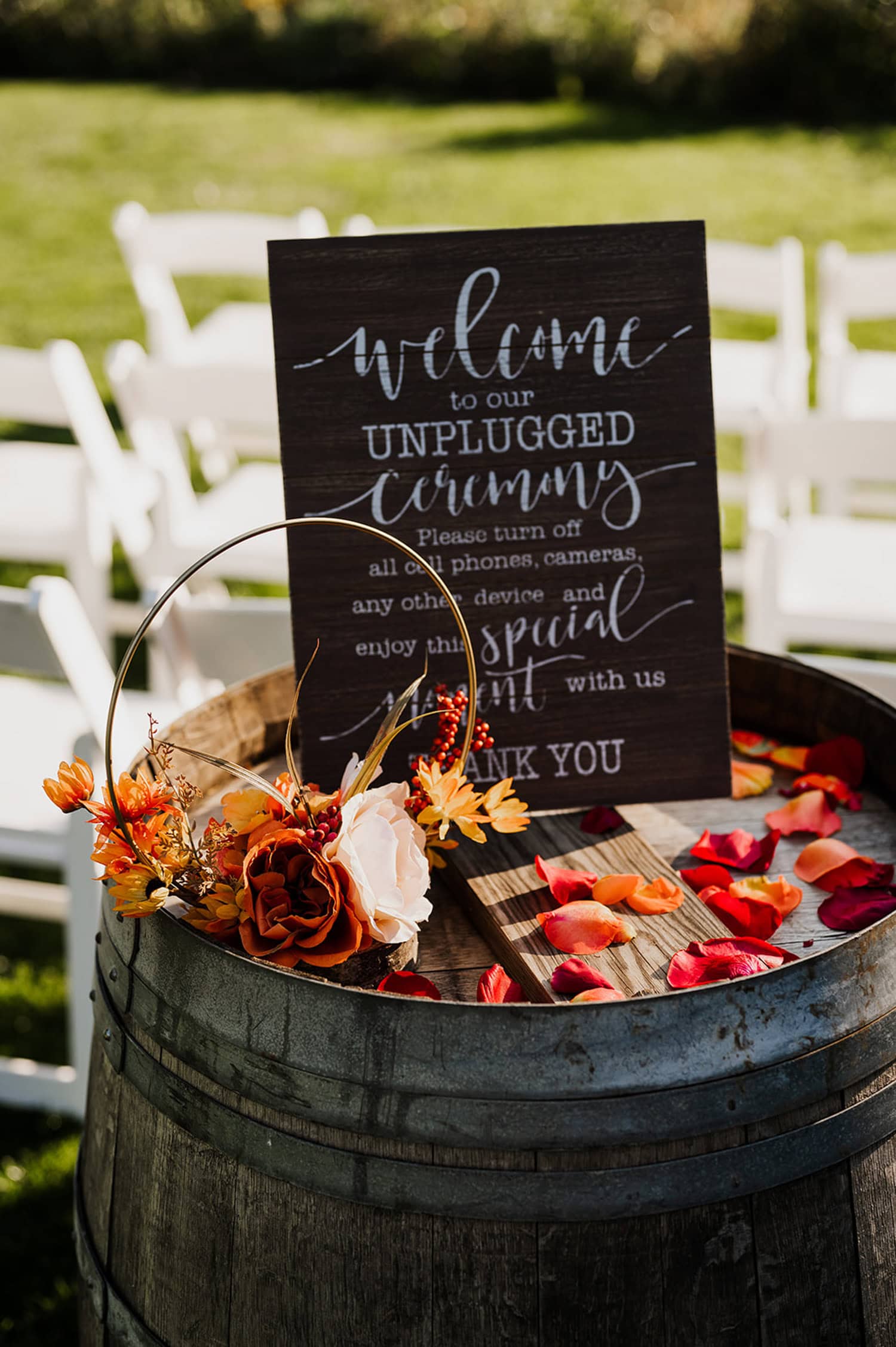 A wooden sign on a barrel with fall flowers and petals welcomes guests to an unplugged ceremony at Gorge Crest Vineyards.