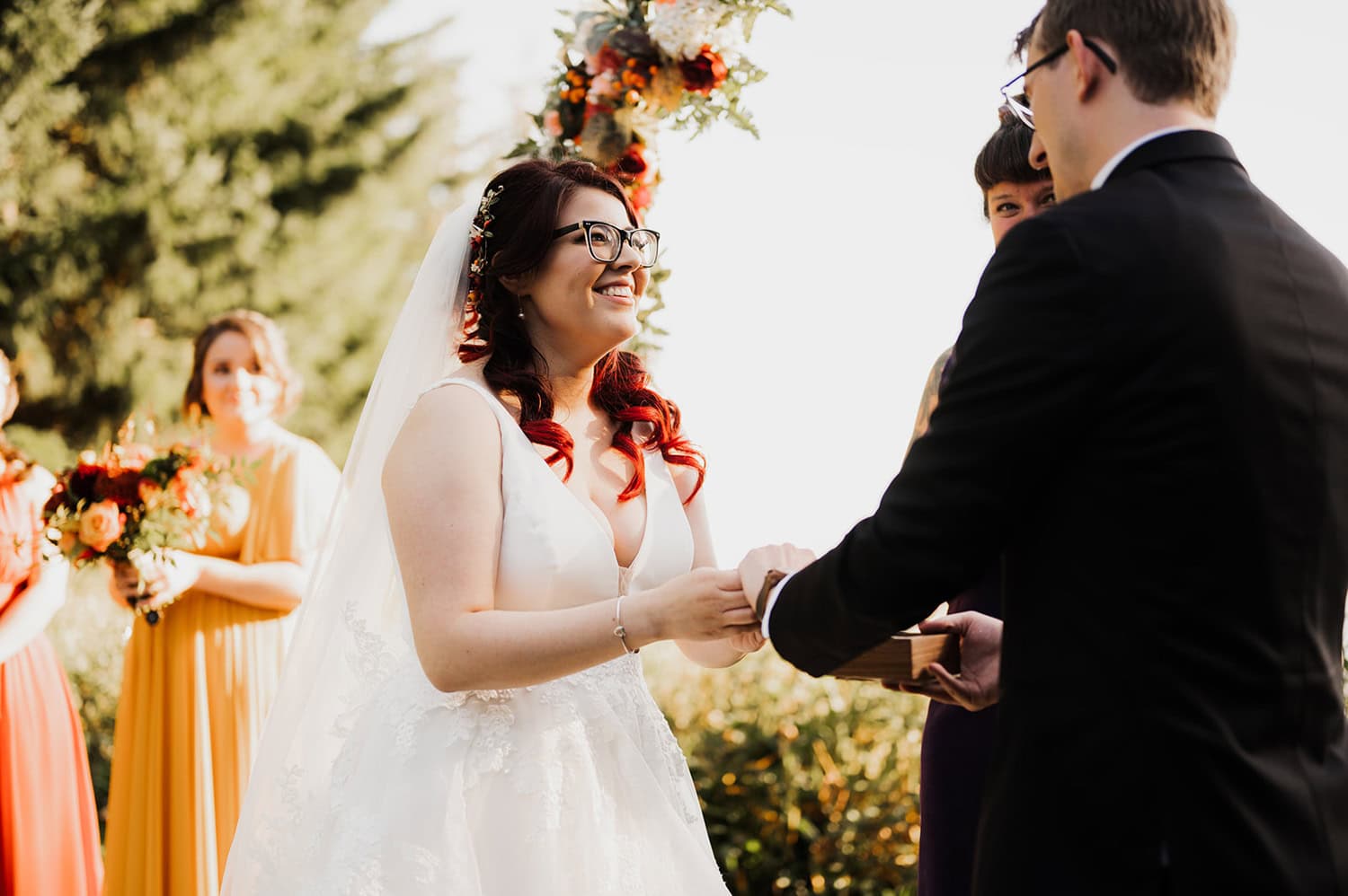 Bride and groom exchanging vows outdoors at Gorge Crest Vineyards, surrounded by bridesmaids and a floral arch.