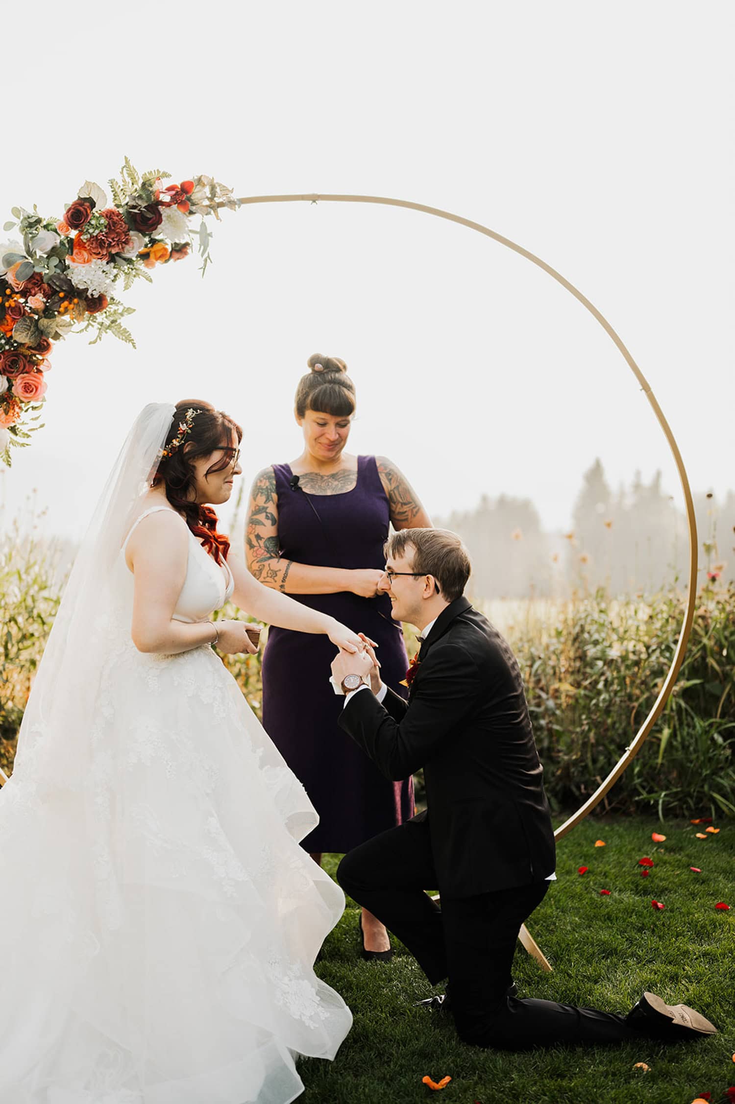 A bride and groom exchanging vows outdoors at Gorge Crest Vineyards, standing under a floral arch with an officiant visible behind them.