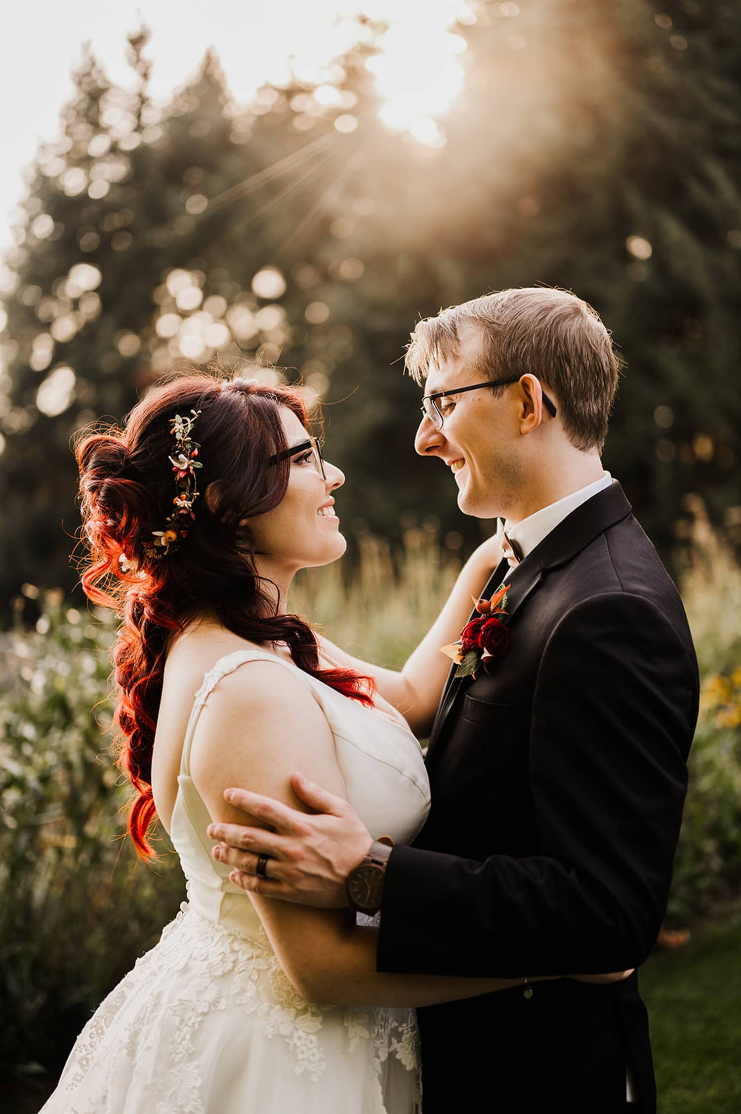 The bride and groom embrace, smiling at each other with sunlight filtering through the trees at Gorge Crest Vineyards.