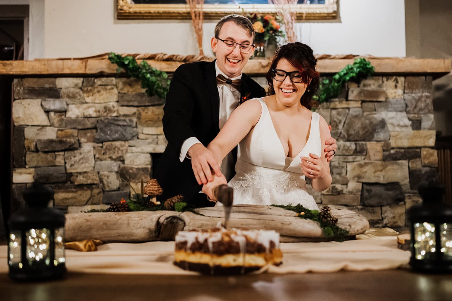 A couple cuts their wedding cake in front of a rustic stone wall decorated with hanging lanterns at Gorge Crest Vineyards.