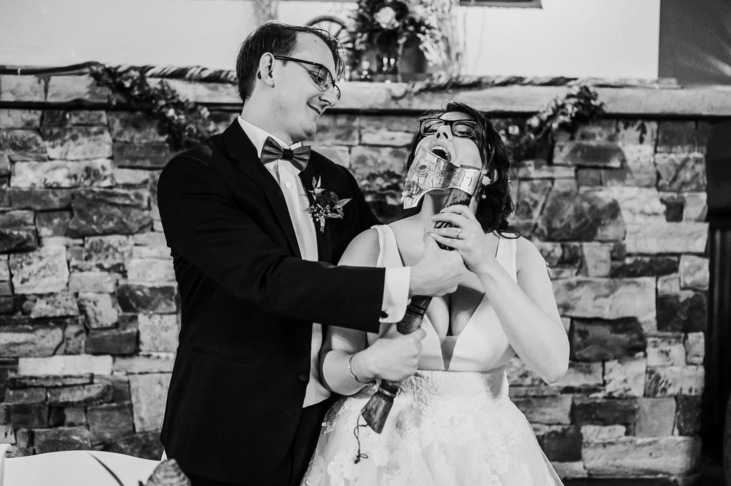A bride and groom playfully hold a medieval helmet on a stick in front of a stone wall at Gorge Crest Vineyards.