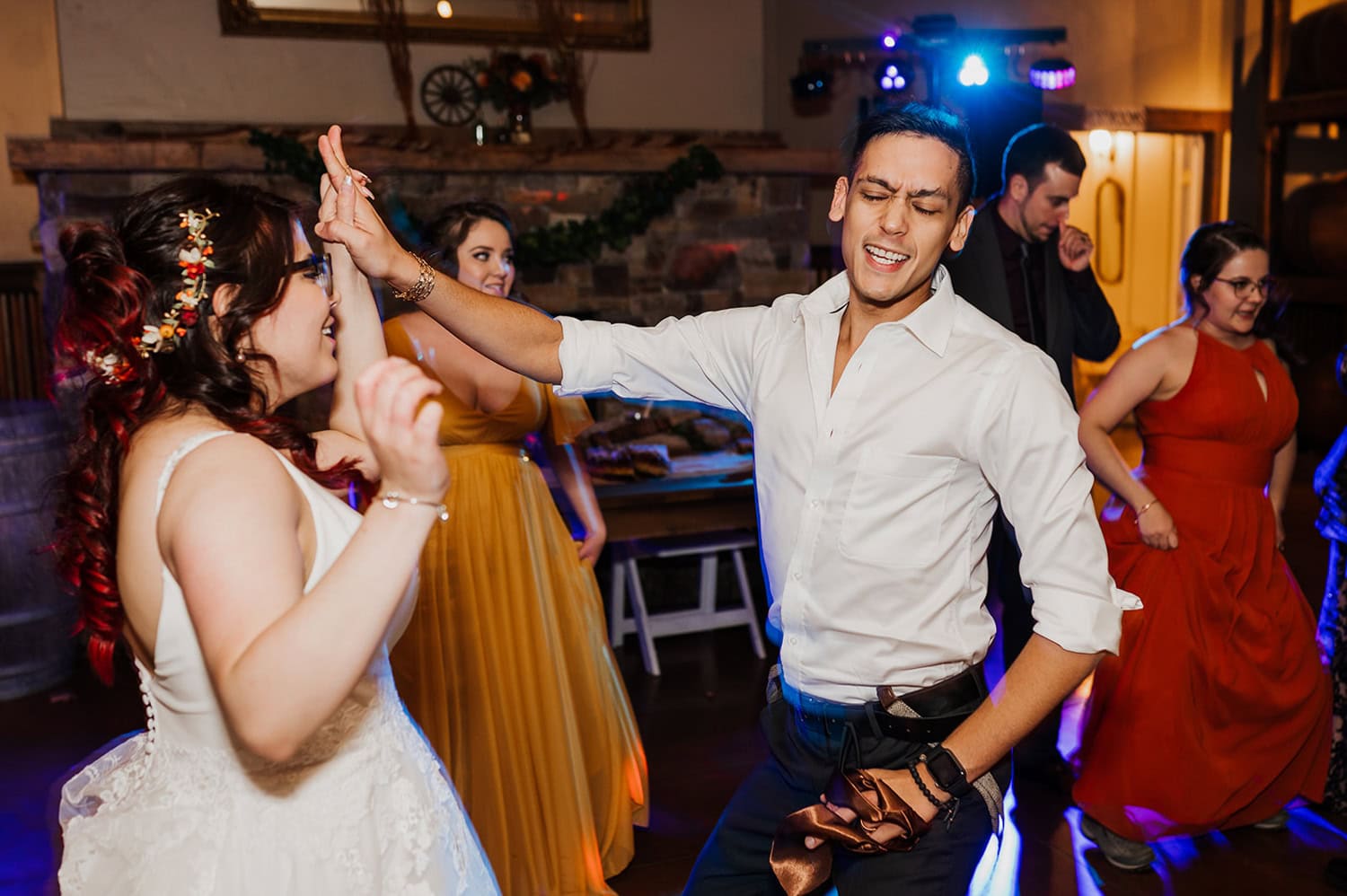 At a lively Gorge Crest Vineyards wedding, guests dance energetically in colorful dresses, creating a joyful atmosphere. A radiant bride twirls gracefully in her wedding dress, adding to the vibrant scene of joy and celebration.