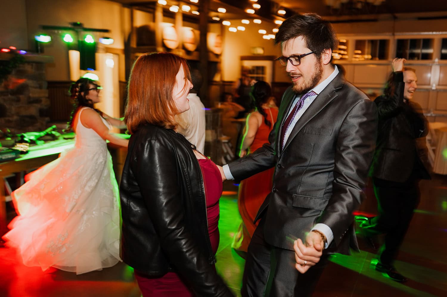 A couple gracefully dances at a lively indoor party, with other guests enjoying the event in the background.