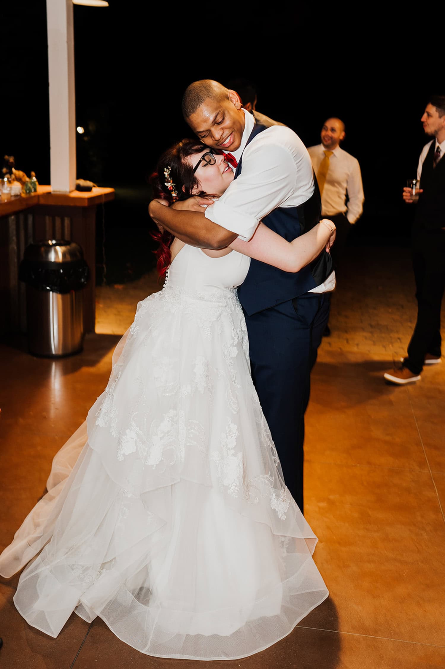 A bride in a white gown hugs a groom in a dark suit on the dance floor at Gorge Crest Vineyards, with joyful guests visible in the background.