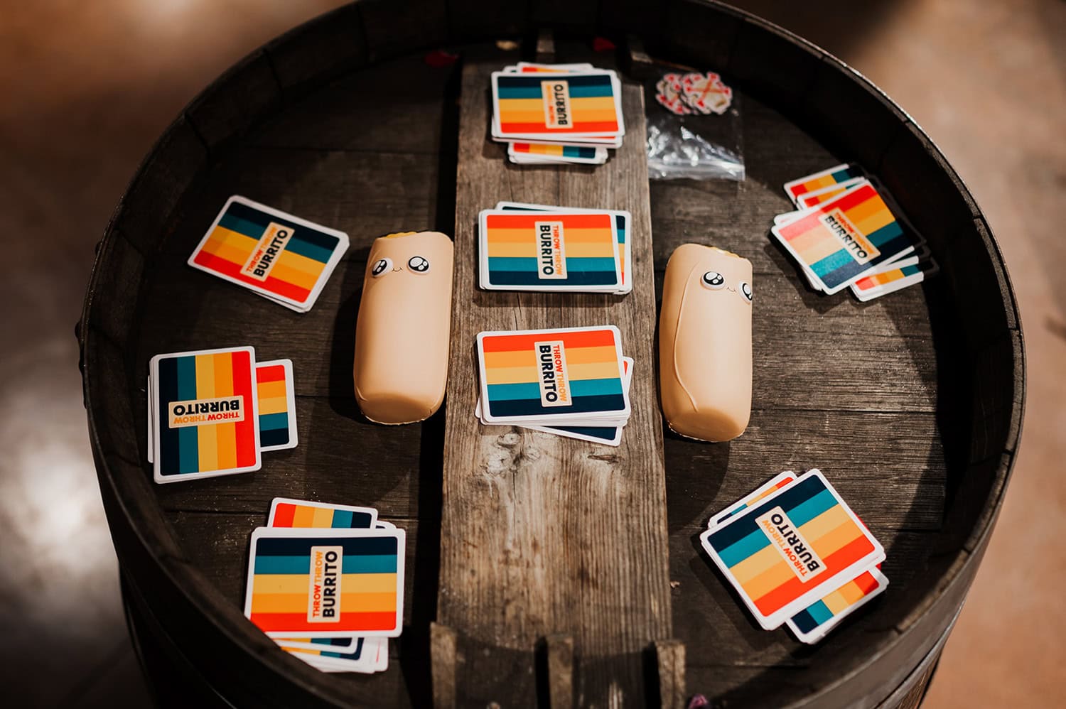 A round wooden table at Gorge Crest Vineyards is decorated with colorful cards and two pillow-like objects resembling burritos with faces, adding a playful element to the wedding setting.