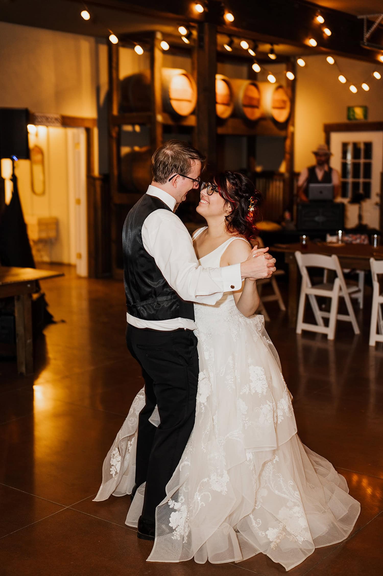 A bride and groom in formal attire dances closely at a warmly lit indoor reception at Gorge Crest Vineyards.