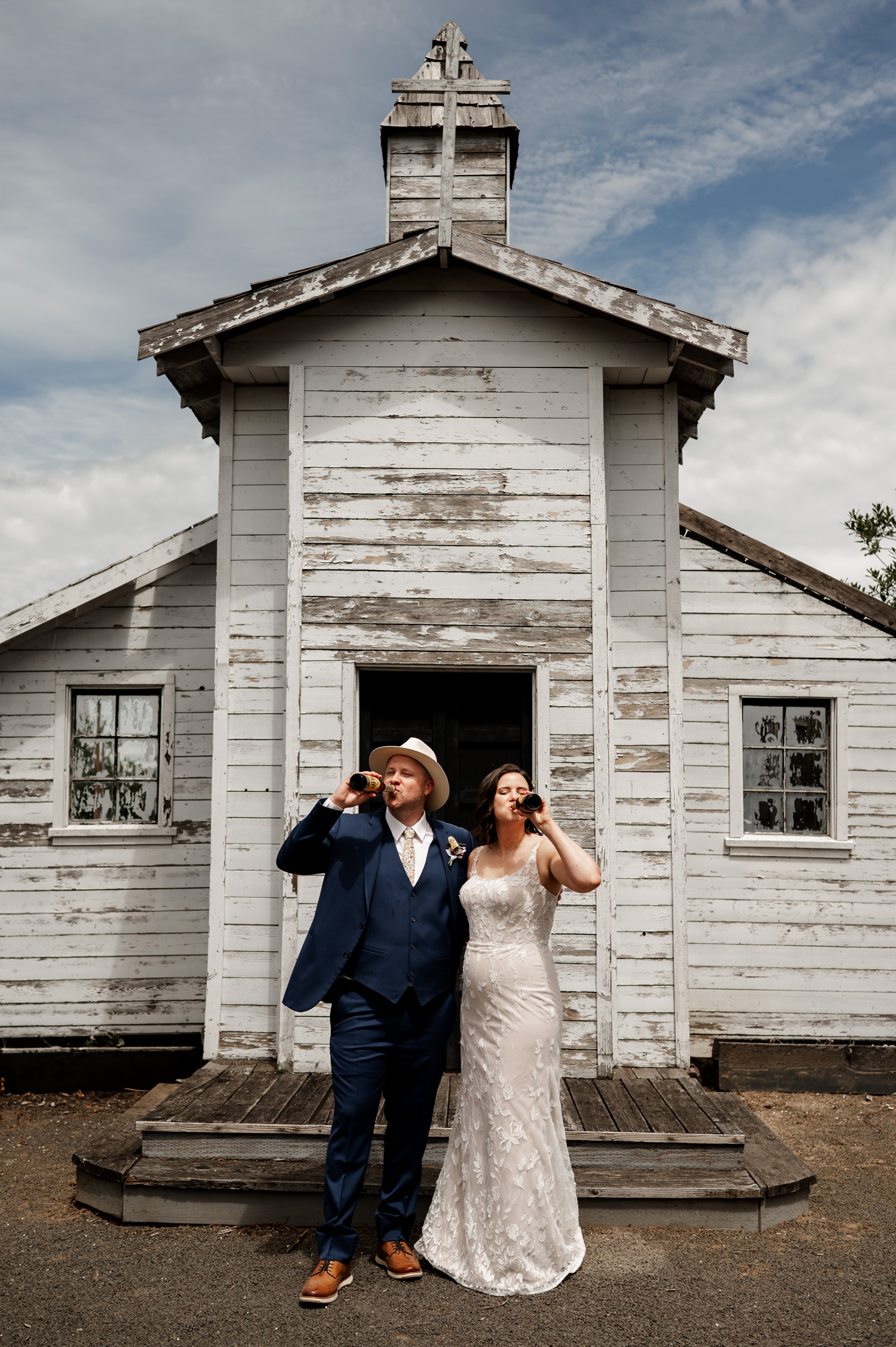 Bride and groom happily sipping beer while posing in front of a rustic white chapel at Rossi Farms.