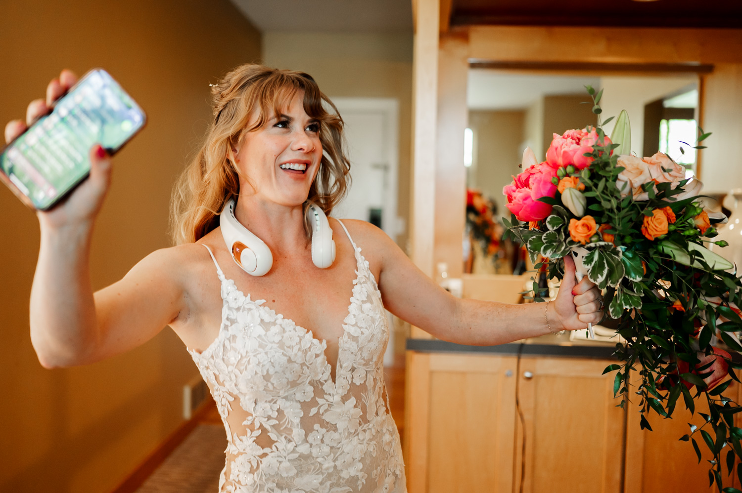 A bride joyfully smiles while wearing headphones, holding her phone and bouquet in a room before her wedding at the Hoyt Arboretum Redwood Deck.
