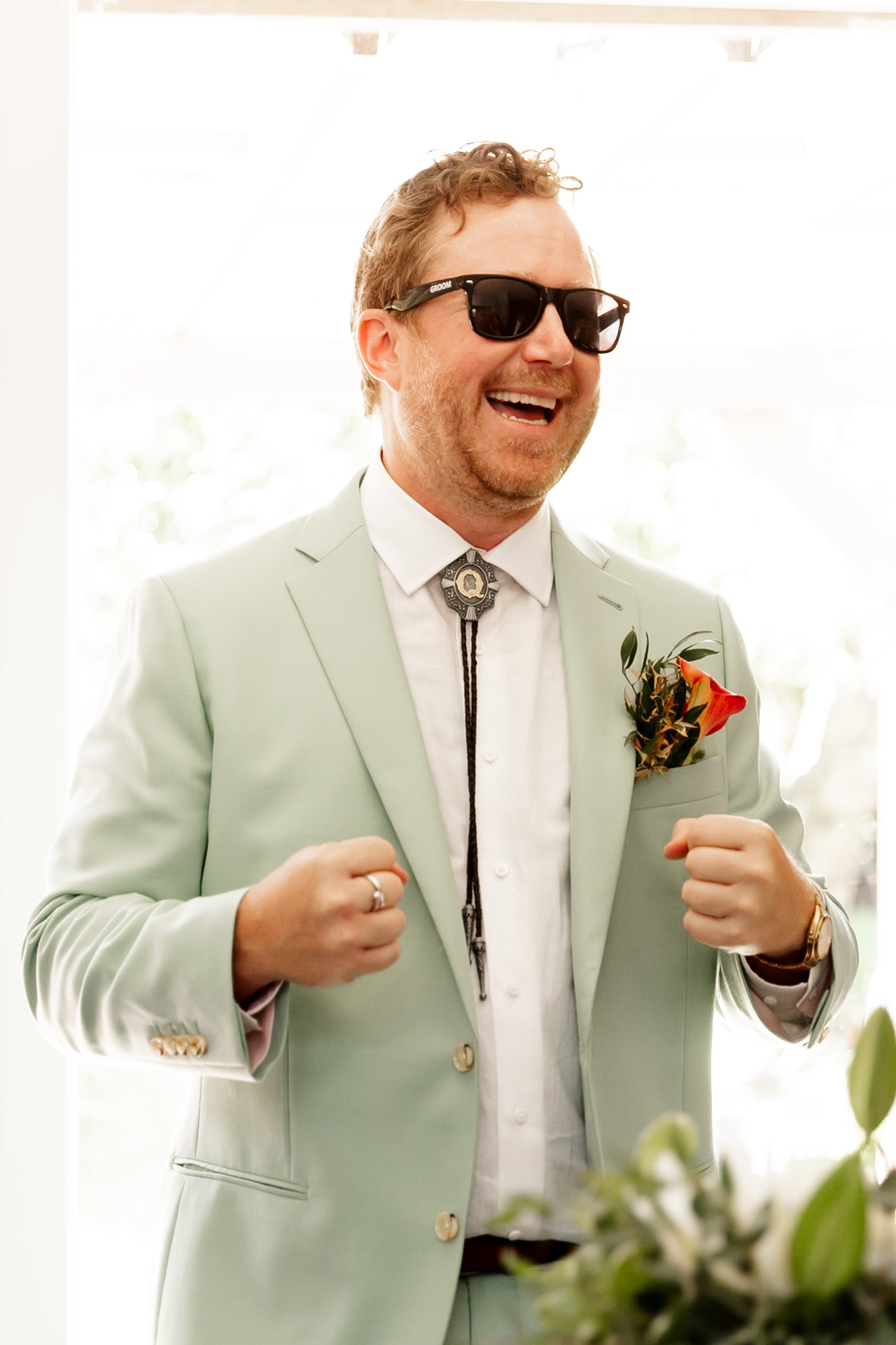 Man in a mint green suit with a bolo tie and sunglasses, smiling with fists slightly raised at the scenic Hoyt Arboretum Redwood Deck.
