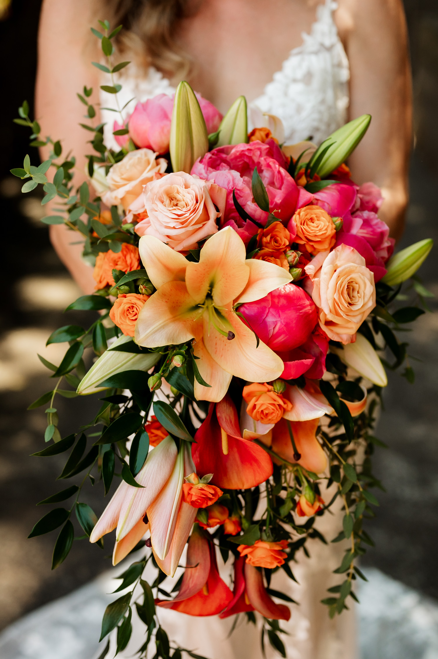 A bride holding a large bouquet with lilies, roses, peonies, and greenery stands on the Hoyt Arboretum Redwood Deck.