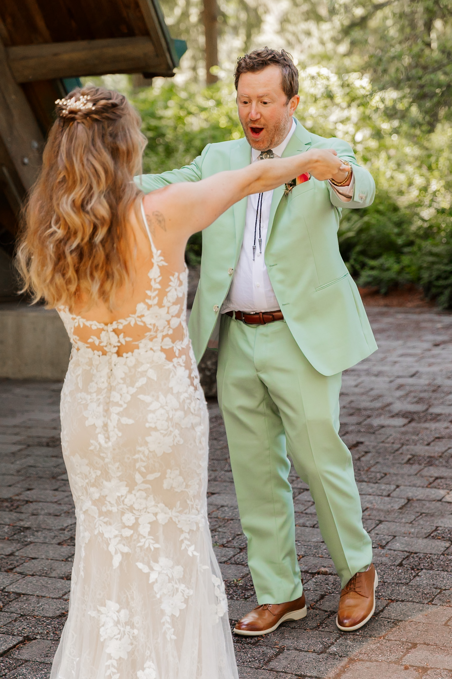 A surprised man in a mint green suit looks at a woman in a lace wedding dress outdoors during their wedding photos at the Hoyt Arboretum Stevens Pavilion.