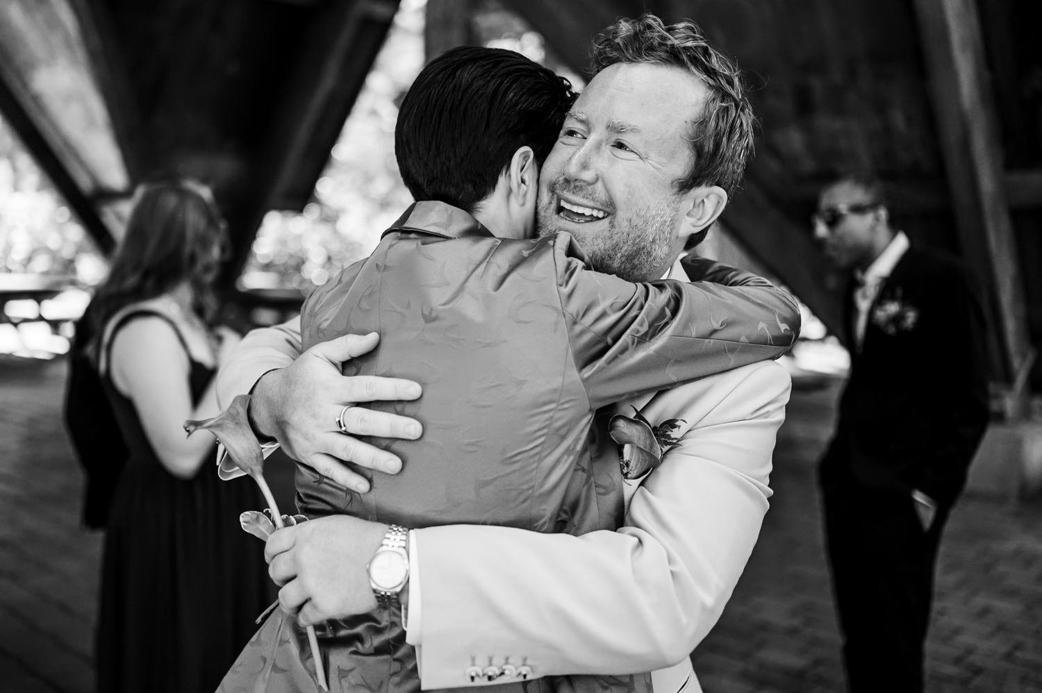 Two people embrace in a hug amidst a joyful crowd at the Stevens Pavilion in Hoyt Arboretum, captured as a memorable wedding photo.