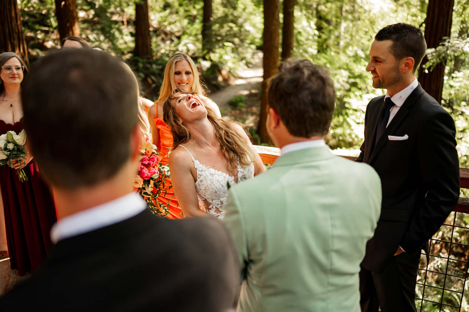 Bride laughing joyfully during the wedding ceremony at the Redwood Deck in Hoyt Arboretum, surrounded by groom and guests.
