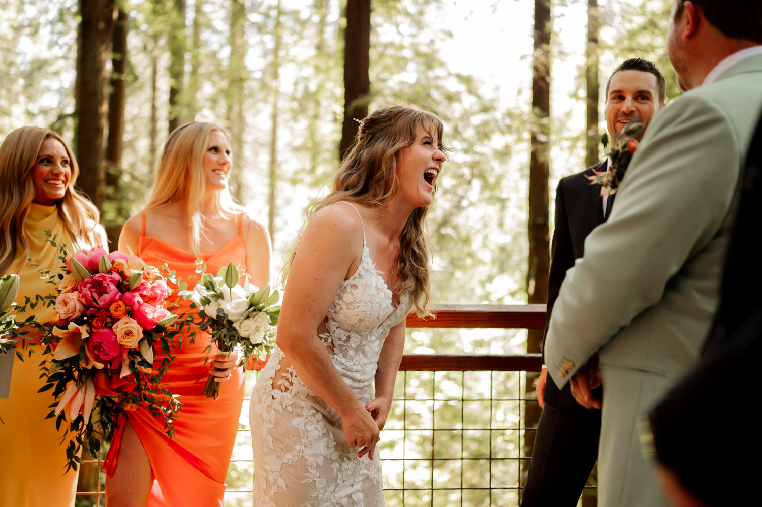 Bride laughing during an outdoor wedding ceremony with the bridal party and a forest background at the Redwood Deck in Hoyt Arboretum.