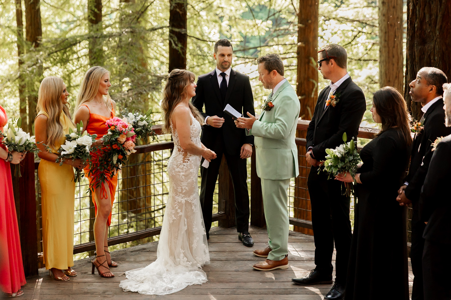 A couple exchanges vows on the Redwood Deck in Hoyt Arboretum, surrounded by towering trees and accompanied by bridesmaids and groomsmen. The forest setting creates a natural backdrop for the wedding ceremony.
