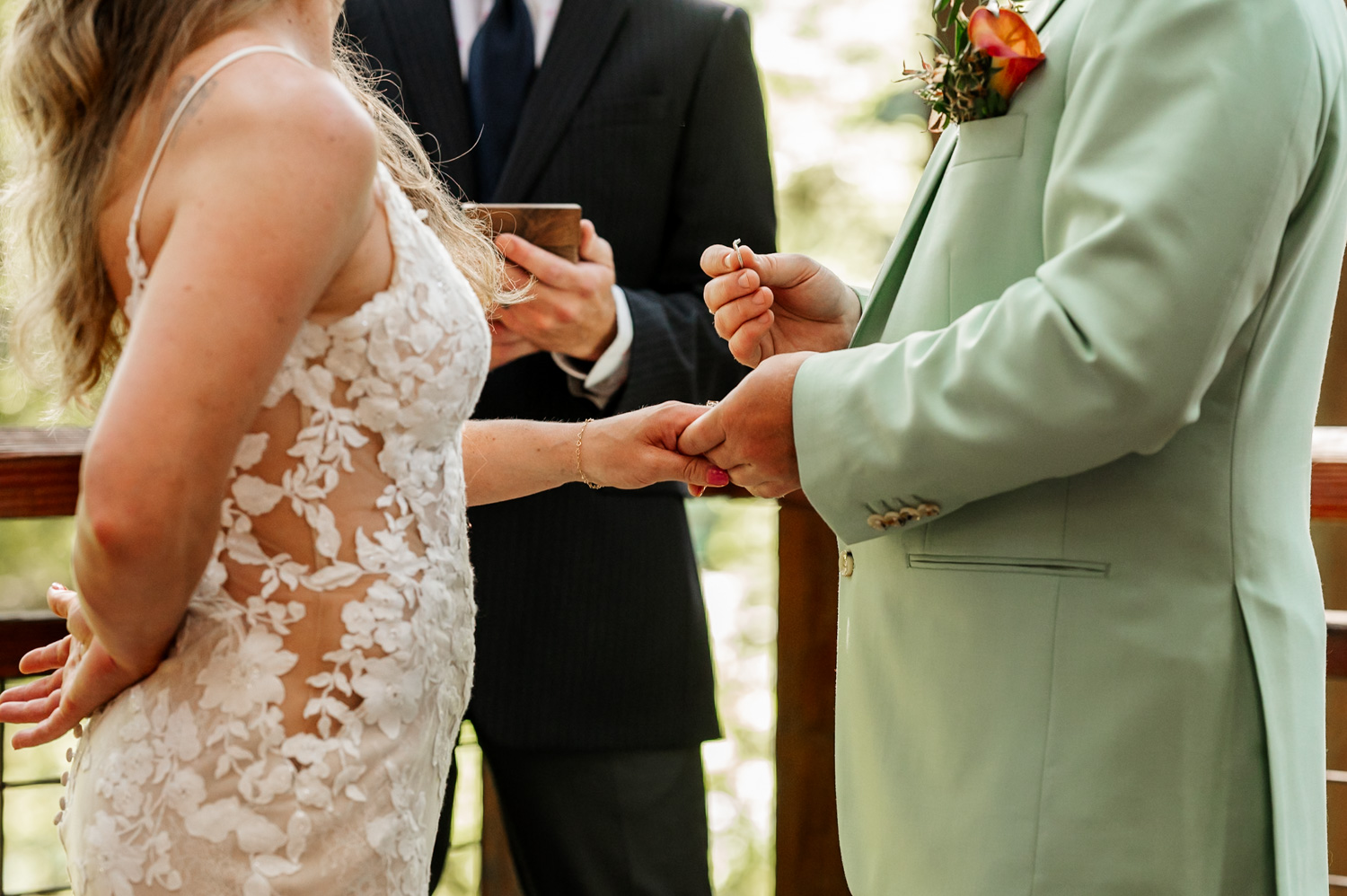 A couple exchanges rings during their wedding ceremony with a suited officiant standing nearby. The setting is the Redwood Deck in Hoyt Arboretum, surrounded by towering trees and natural beauty.