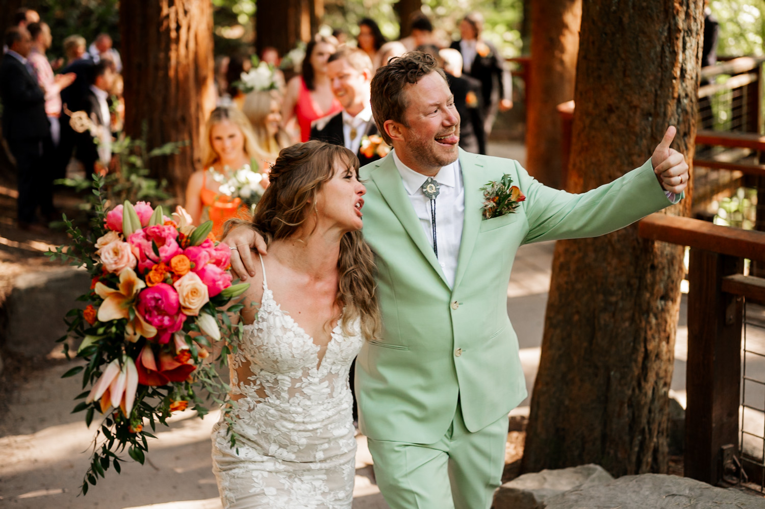 The bride and groom celebrate joyfully outdoors at the Redwood Deck in Hoyt Arboretum; she holds a bouquet, and he gives a thumbs up, capturing a perfect moment for their wedding ceremony photos.
