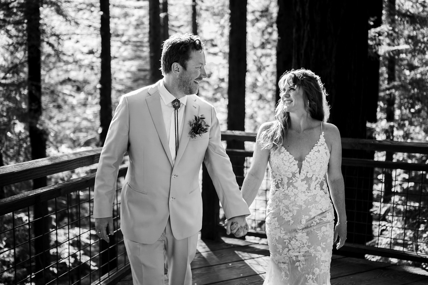 Bride and groom walking hand in hand on a wooded path in wedding attire, smiling as they capture wedding photos at the Hoyt Arboretum Redwood deck.