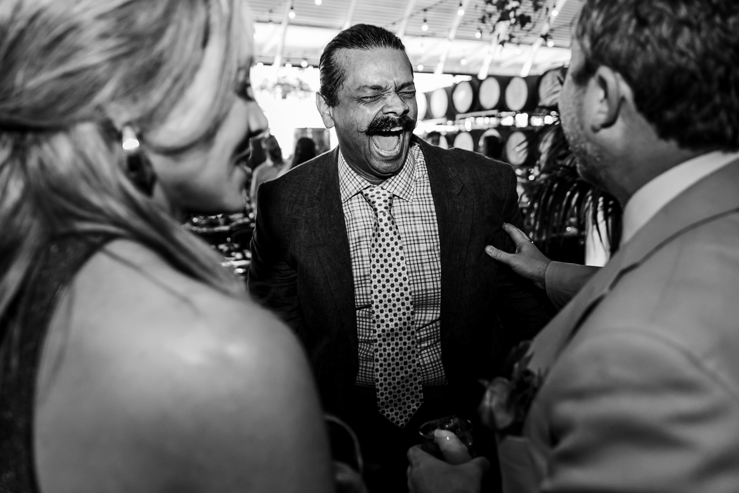 A man laughing energetically while chatting with a man and a woman at a lively wedding reception at Coopers Hall.