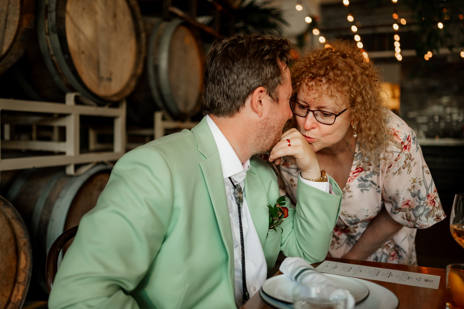 A couple embraces tenderly at Coopers Hall, with wine barrels and soft ambient lighting enhancing the wedding reception setting.