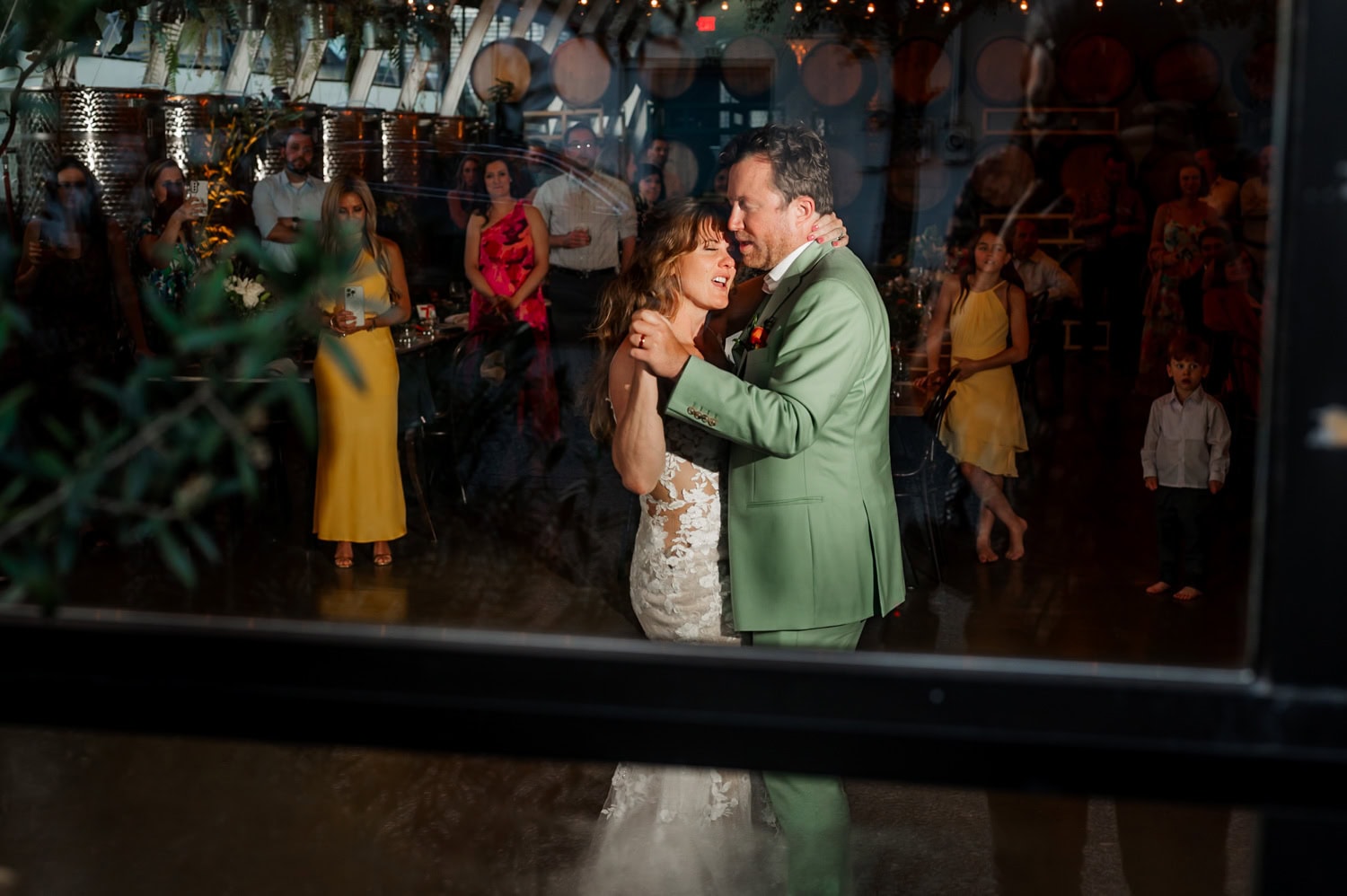 Bride and groom dance joyfully at their wedding reception at Coopers Hall, with guests in colorful attire seated around them under warm venue lights.