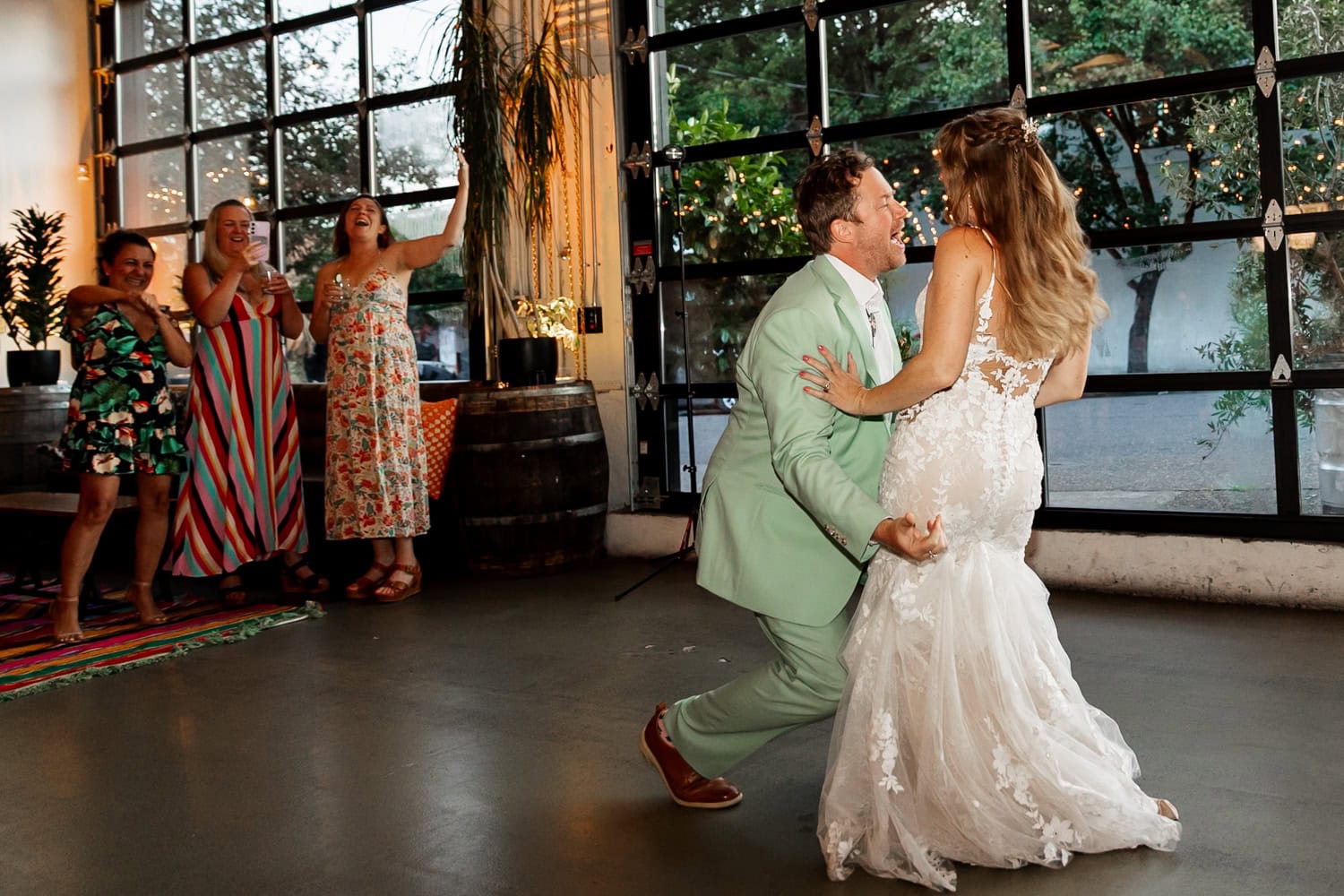 A couple in wedding attire dances joyfully while guests watch and cheer inside the bright venue of Coopers Hall.