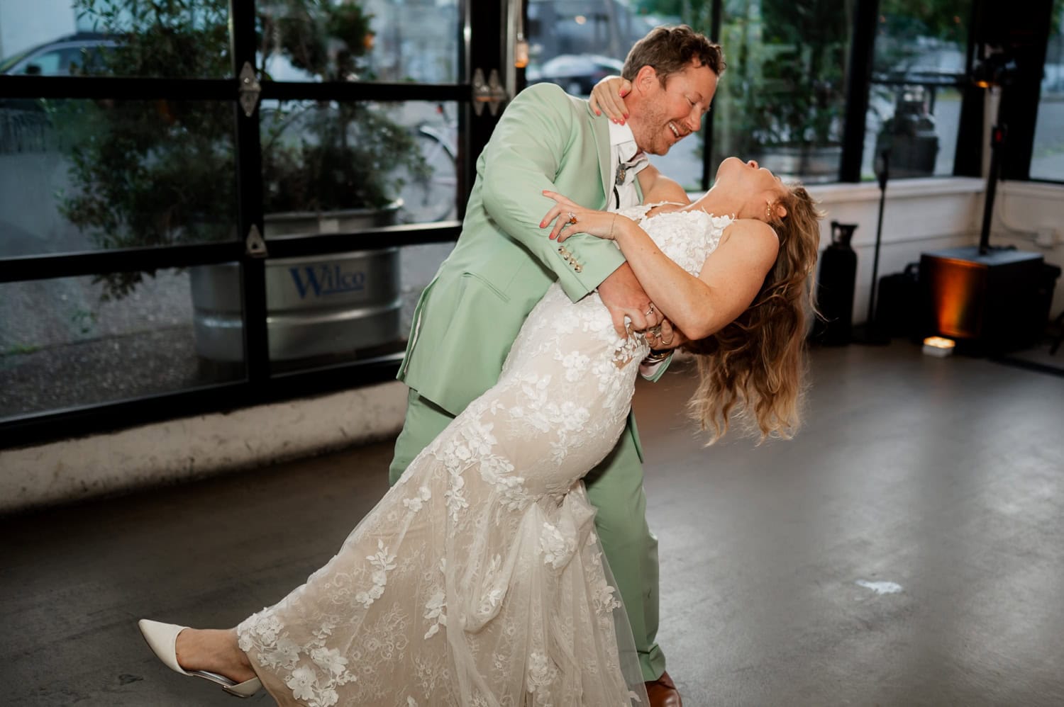 A couple in formal attire dances, with the man gently dipping the woman in a joyful indoor setting at a wedding reception at Coopers Hall.