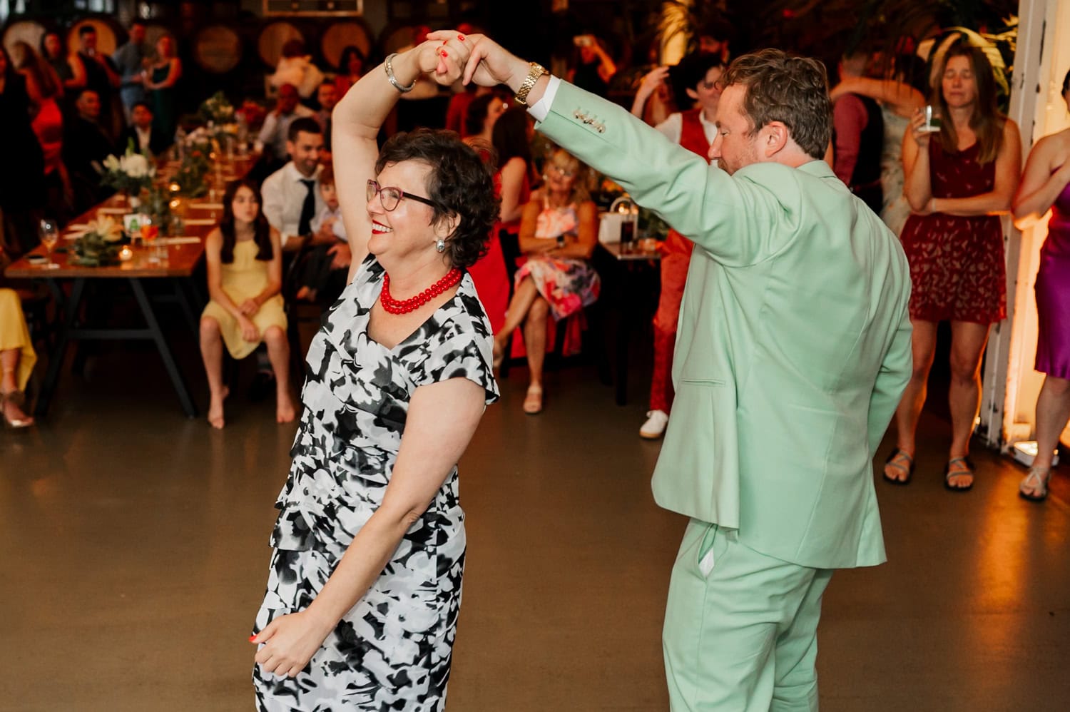 A man in a light green suit and a woman in a black-and-white dress dance joyfully at a wedding reception at Coopers Hall.