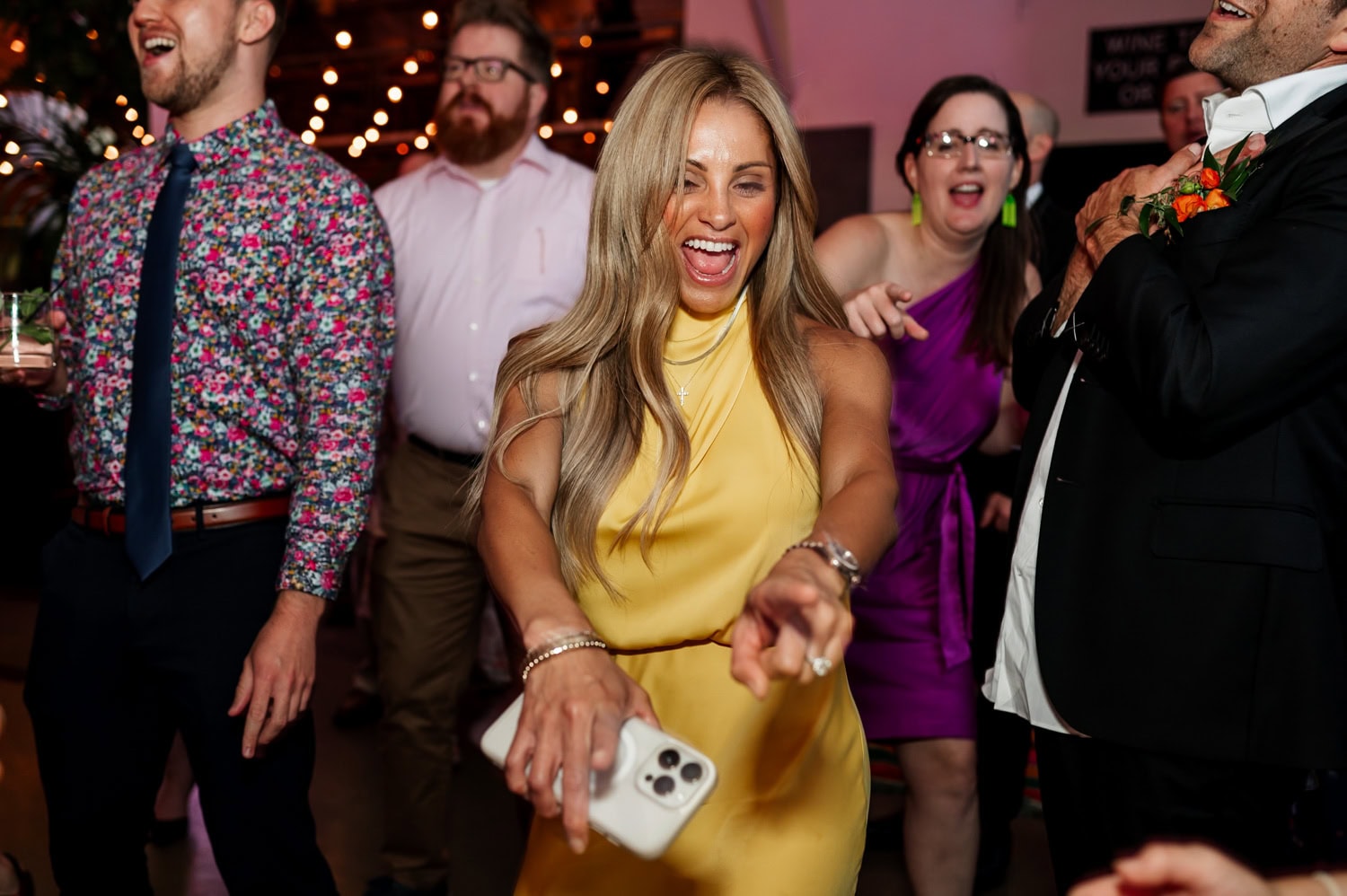 A woman in a yellow dress dances joyfully at a wedding reception at Coopers Hall, surrounded by guests wearing festive attire.