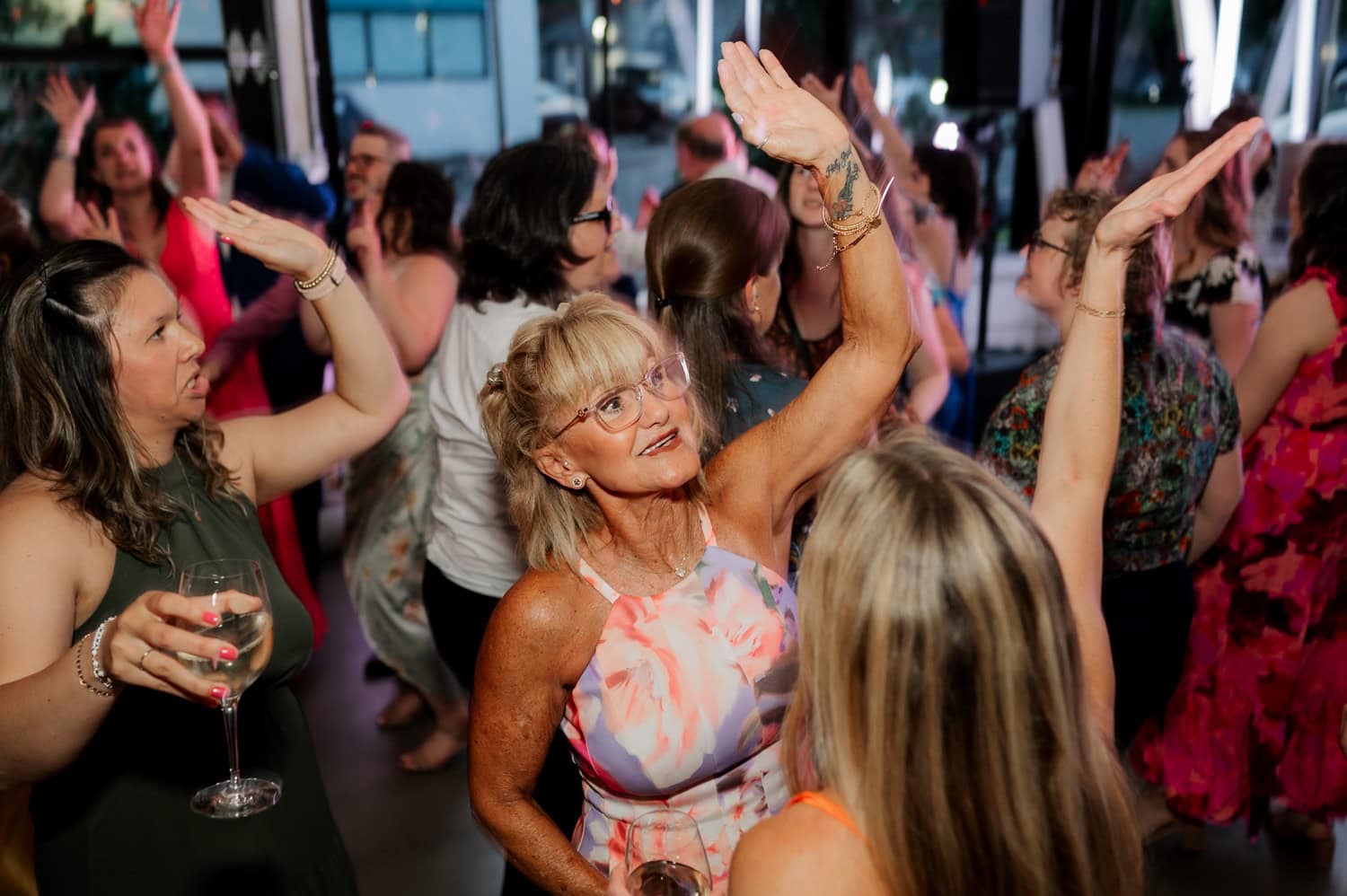 Guests dance and hold drinks at a lively indoor wedding reception at Coopers Hall.