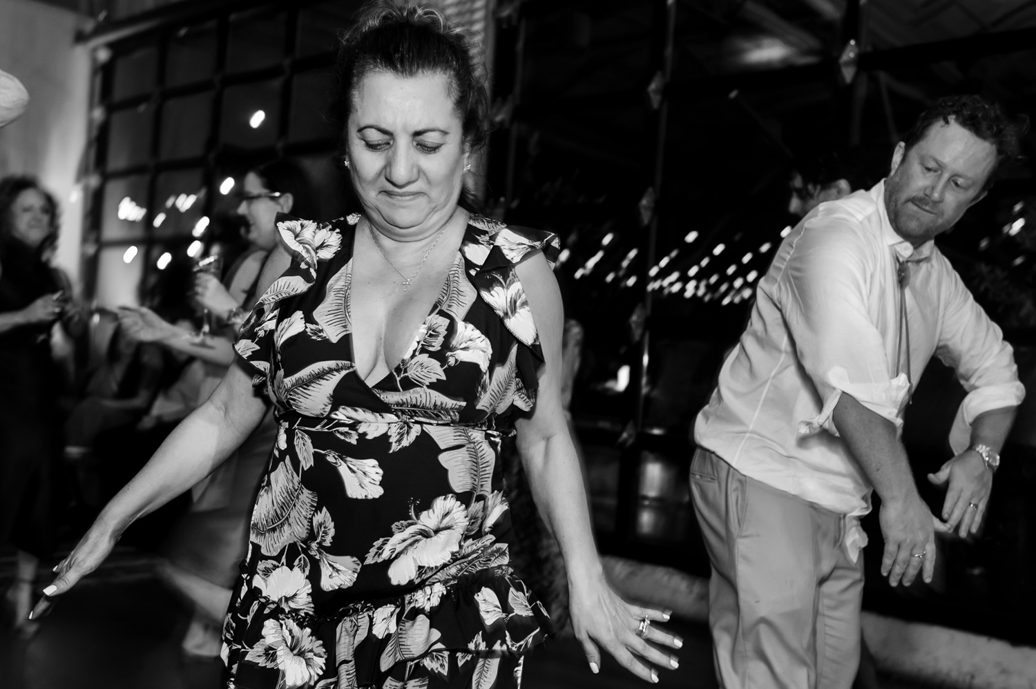 A woman in a floral dress and a man dance energetically at a lively wedding reception at Coopers Hall, captured in black and white.