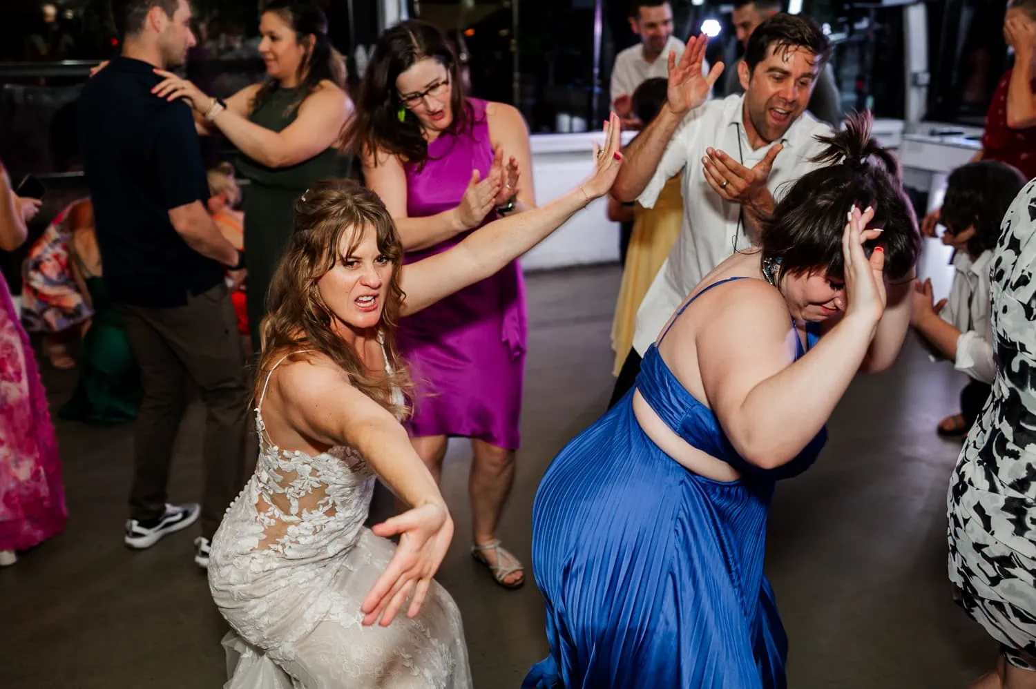 A lively wedding reception at Coopers Hall, with guests energetically dancing. A woman in a white dress stands in the foreground, striking a playful pose.