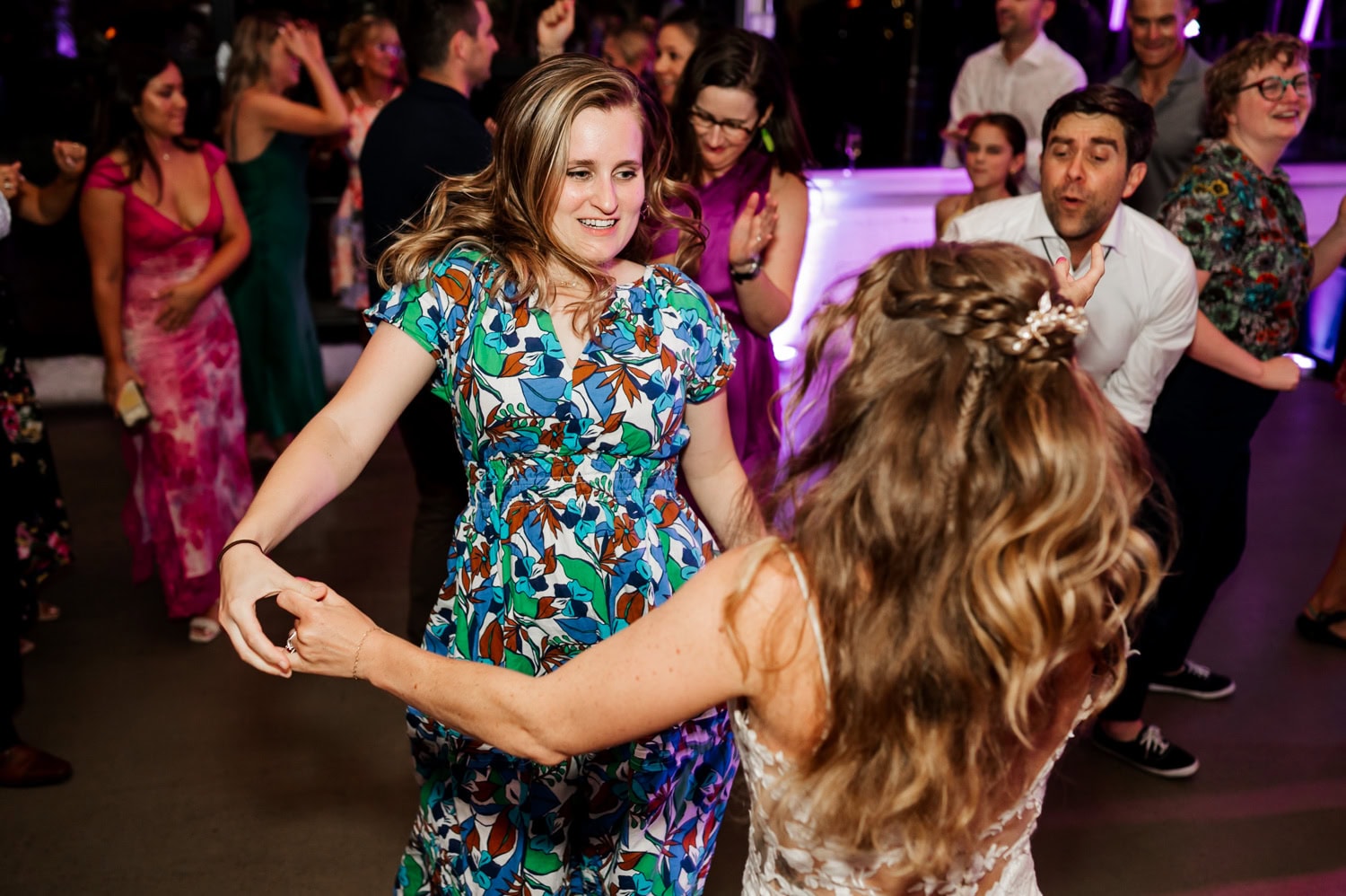 Guests dancing energetically at a wedding reception at Coopers Hall, with colorful lights and elegant attire visible in the background.
