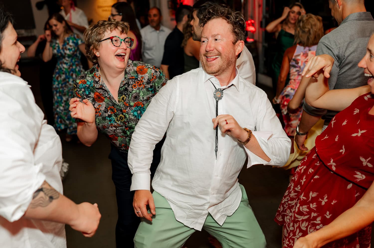 People dancing joyfully at a wedding reception in Coopers Hall, wearing colorful outfits and displaying smiling faces.