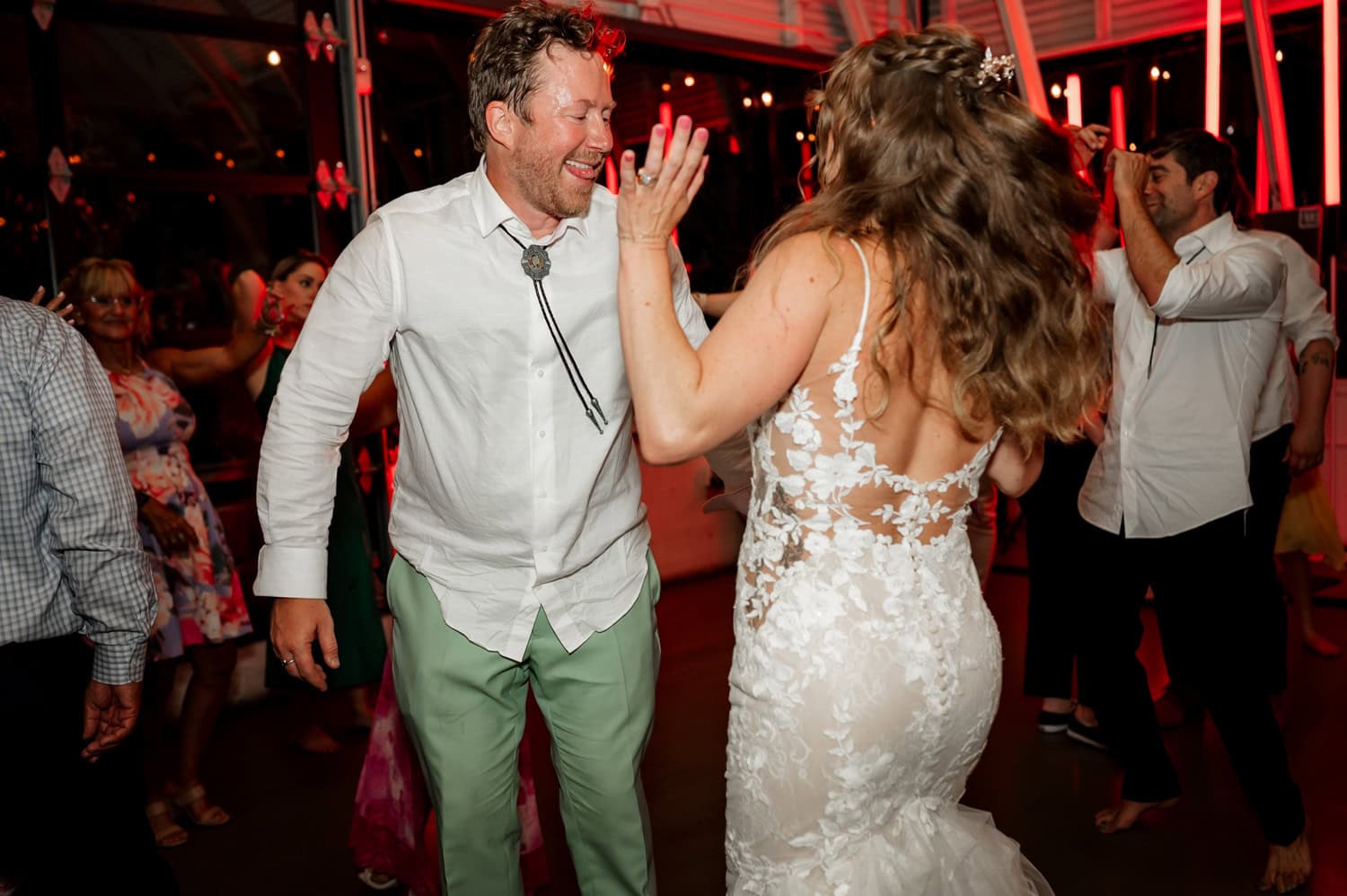 A couple in formal attire dances joyfully at a lively wedding reception at Coopers Hall, with people visible in the background.