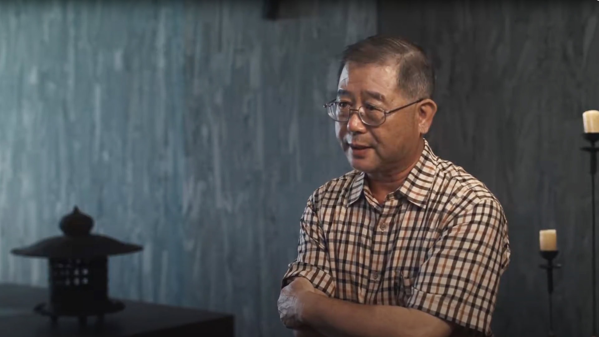 專業人物形象拍攝｜中部專業影像作品｜奇力克影像工作室 KYRIC STUDIO。室內環境人物肖像，穿著格紋襯衫的中年男性受訪者配戴眼鏡，背景為藍灰色牆面與東方擺飾，專業燈光營造溫暖質感，適合企業形象、訪談紀錄等應用。