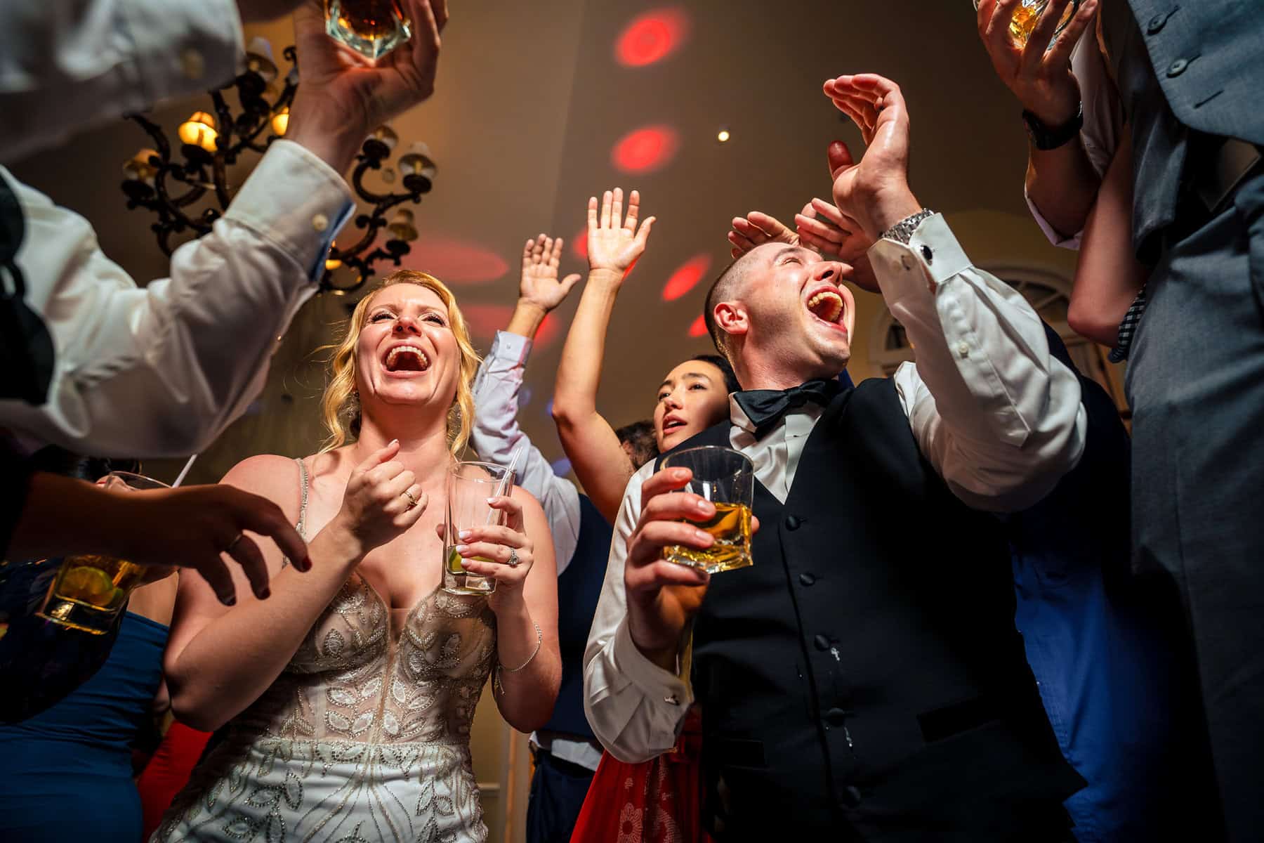 Bride and groom laughing and celebrating on the dance floor surrounded by guests during a lively wedding reception, captured by a CT wedding photographer