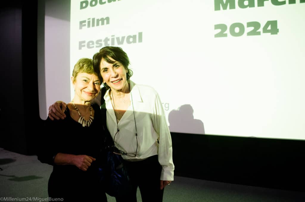 Sourire de deux femmes lors d'un festival de cinéma, devant un écran projetant "La Nostalgie de l'Ailleurs".