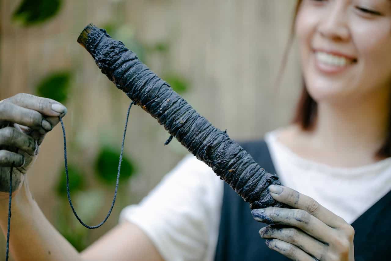 about-us-01 A woman displays a skein of freshly dyed indigo yarn, showcasing traditional dyeing techniques.