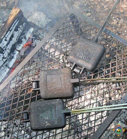 3 pie irons on a grate over a campfire