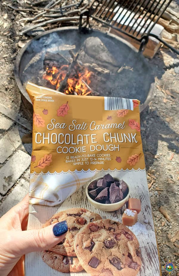 a package of caramel chocolate chunk cookie dough behind held with a campfire in the background