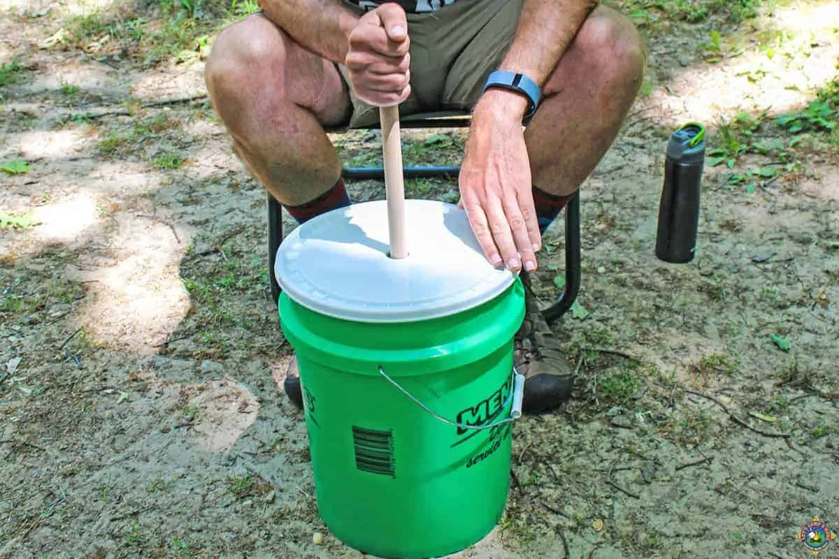 person using the hand crank on a handmade washing machine while camping