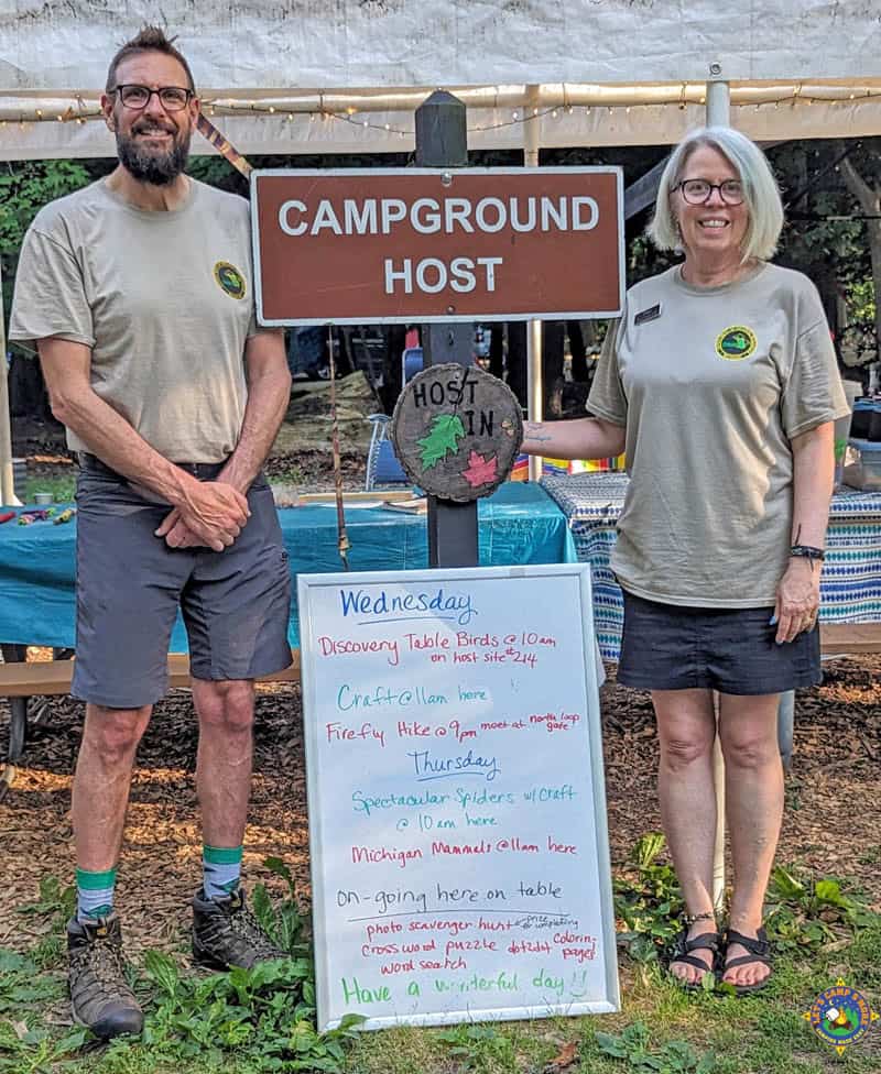 couple standing near a campground host sign
