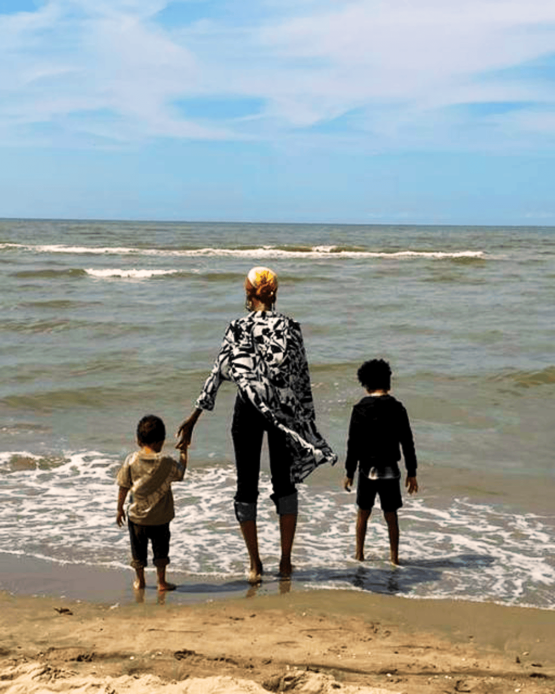 woman and two kids on the beach looking out over the ocean